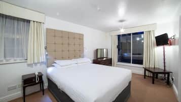 Una camera d'albergo con un letto grande, un comodino, una televisione e una finestra con tende.