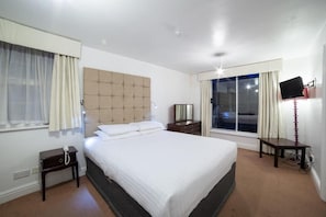 Ein Hotelzimmer mit einem großen Bett, einem Nachttisch, einem Fernseher und einem Fenster mit Vorhängen.