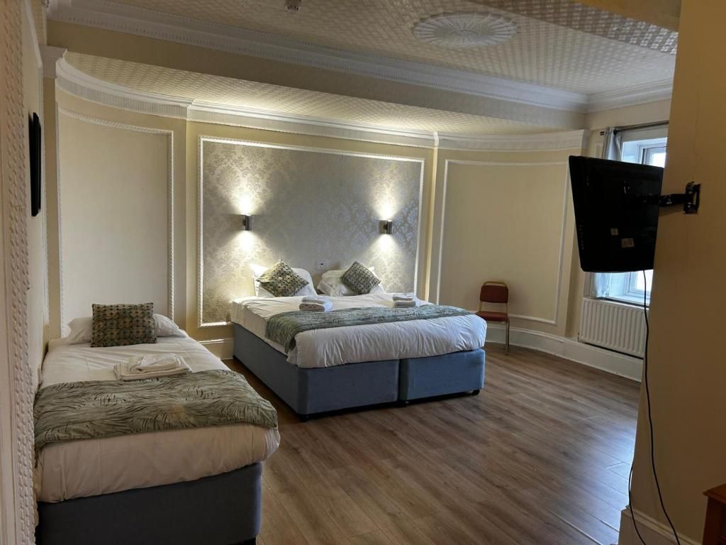 A bedroom with two beds, a large wall-mounted TV, and a ceiling with a decorative pattern.