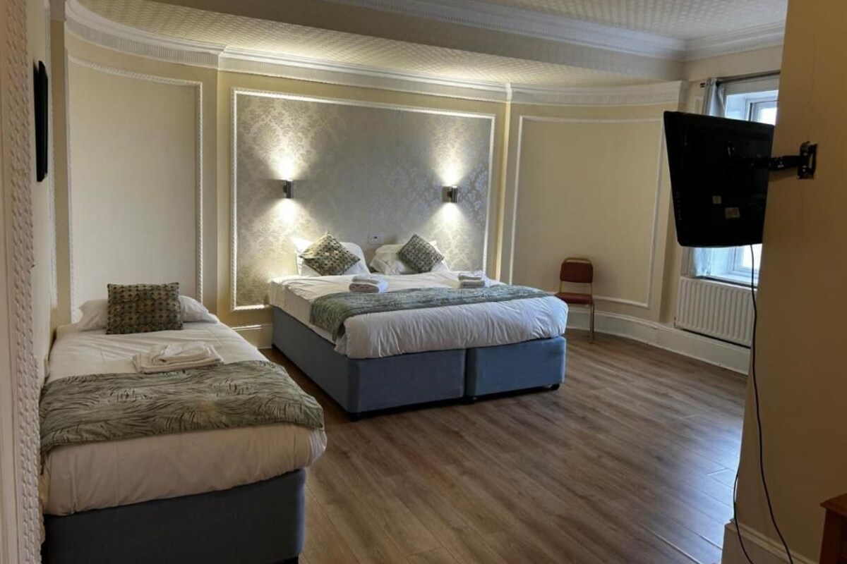 Ein Schlafzimmer mit zwei Betten, einem großen, an der Wand befestigten Fernseher und einer Decke mit Dekor.
