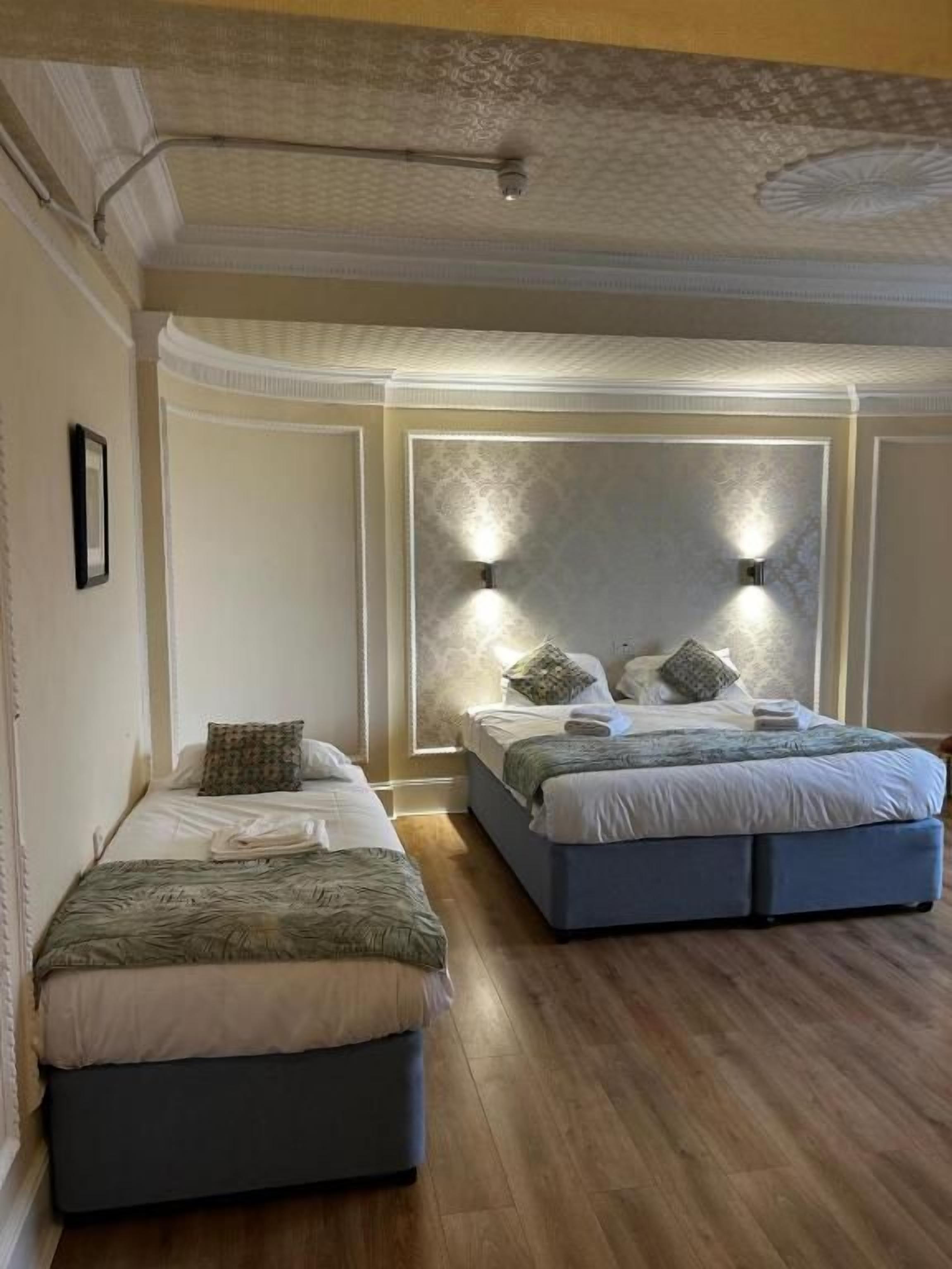 Un dormitorio con dos camas, un techo decorativo y una lámpara fijada a la pared.