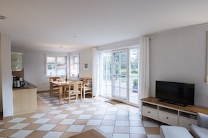 Ein Wohnzimmer mit Fernseher, einer Couch, einem Esstisch mit Stühlen und einer Küchenzeile mit Kaffeemaschine.