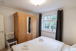 Ein Schlafzimmer mit einem Bett, einem Holzschrank, einem Stuhl und einem Fenster mit Vorhängen.