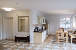 A compact kitchen with a dining area, a bench, and a window with curtains. - House on the Bodden shore (Born a. Darß)
