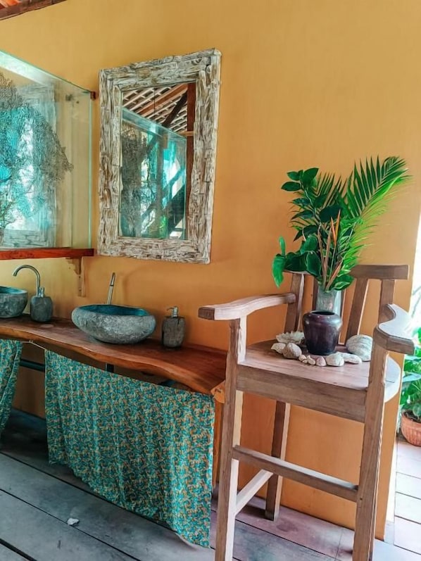 A wooden chair with a potted plant beside it, a stone sink, and a mirror on the wall. - Alaya Ecolodge (Buleleng)