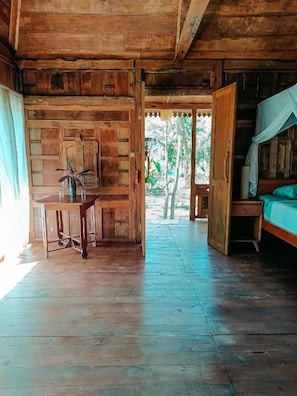 A wooden cabin interior with a bed, a table, and a door leading outside. - Alaya Ecolodge (Buleleng)