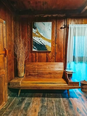 Una habitación de madera con una cama, un cuadro y una ventana con cortinas.