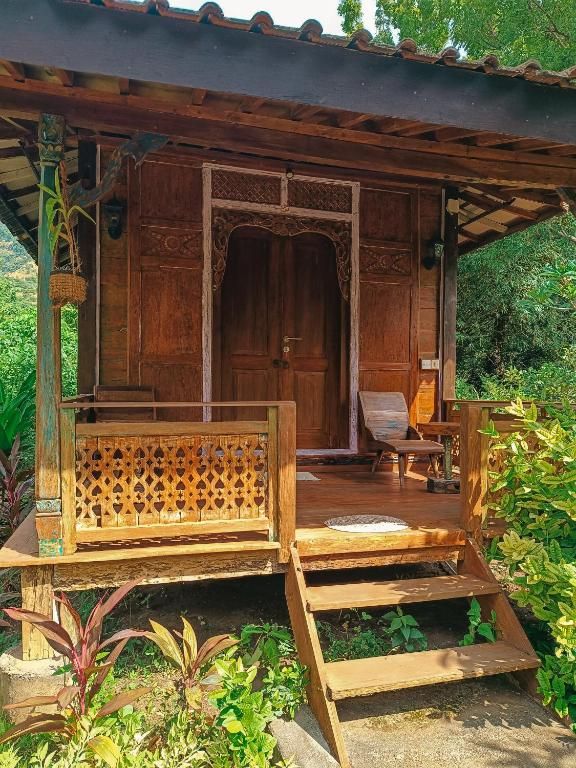 A wooden structure with a bench and a door, surrounded by greenery.