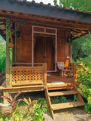 A wooden structure with a bench and a door, surrounded by greenery. - Alaya Ecolodge (Pemuteran)
