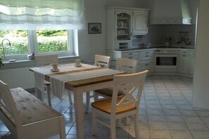 A kitchen with white cabinetry, a dining table with chairs, and a view of greenery outside. - Holiday apartment in Malkendorf with Wi-Fi (Malkendorf)