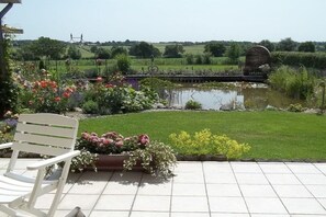 A garden patio with a white chair, a pond, and a view of a rural landscape. - Holiday apartment in Malkendorf with Wi-Fi (Malkendorf)