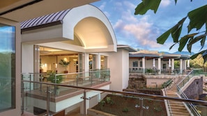 Um hotel moderno com varanda de vidro, um pátio ajardinado e vista para as montanhas.