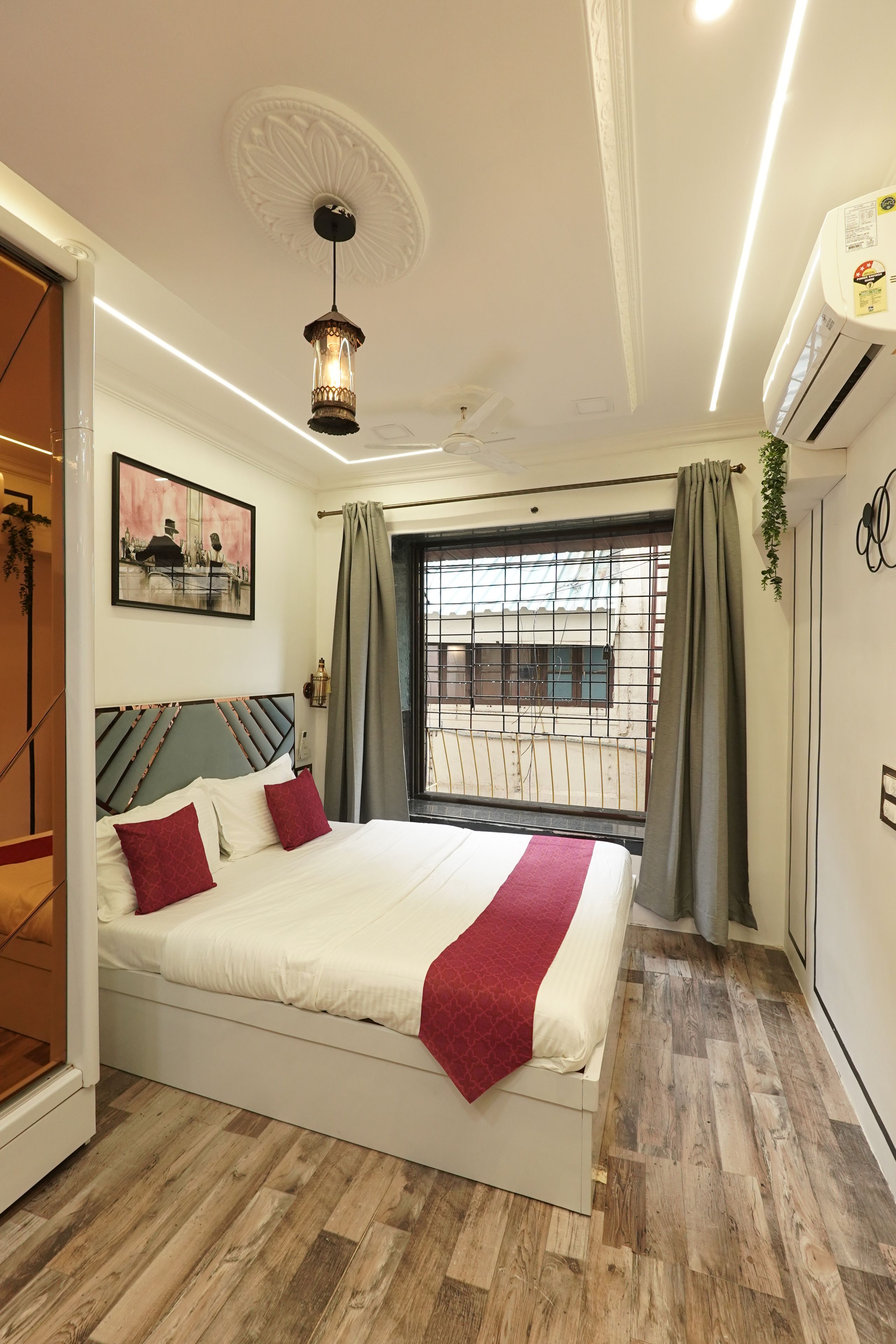 A modern bedroom with a large bed, a window with curtains, a ceiling fan, and a wall-mounted air conditioner.