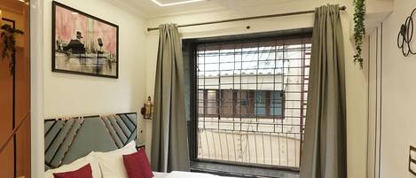 A modern bedroom with a large bed, a window with curtains, a ceiling fan, and a wall-mounted air conditioner.