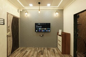A room with a mounted television displaying a streaming service interface, a wooden door, and a reception desk. - Grace Stylish - Cozy 1-Bedroom Stay in Bandra West (Mumbai)