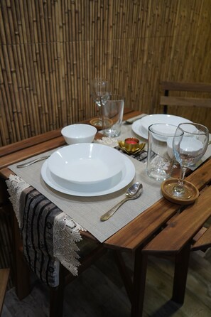 A wooden dining table set with white plates, a spoon, a glass, and a candle holder. - Grace Stylish - Cozy 1-Bedroom Stay in Bandra West (Mumbai)