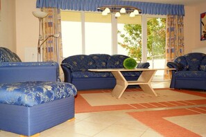 A living room with blue patterned sofas, a wooden coffee table, and a large window with curtains. - Holiday apartment with 2 bedrooms (Ostseebad Boltenhagen)