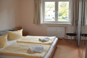 Ein Hotelzimmer mit zwei Betten, einem Heizkörper, einem Fenster mit Vorhängen und einem Sessel.