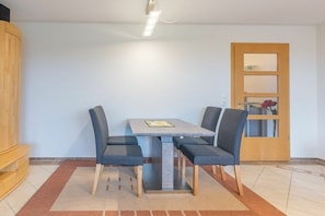 Ein Essbereich mit einem Tisch, vier Stühlen, einem Holzschrank und einer Tür mit Spiegel.