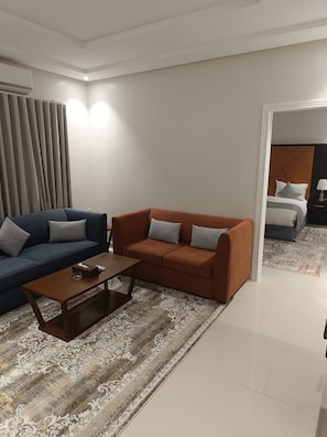 A modern living room with a blue sofa, an orange sofa, and a coffee table. - Best House Granada (Riyadh)