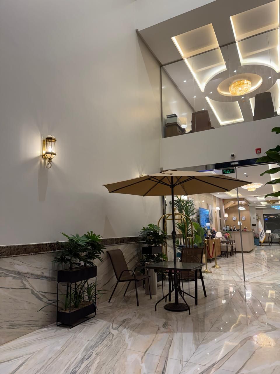 A lobby with a marble floor, a table with chairs, a large umbrella, and wall-mounted lighting.