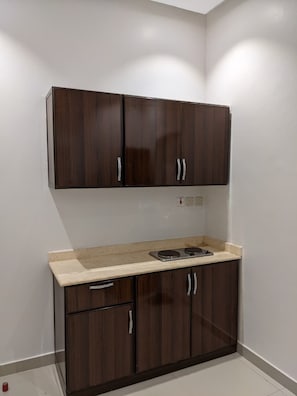 A kitchenette with dark wood cabinets, a white countertop, and a built-in stove. - Best House Granada (Riyadh)