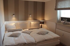A bedroom with a bed, pillows, a bedside lamp, and a window with a curtain. - Holiday apartment in Sylt with 2 bedrooms (Sylt \/ OT Westerland)