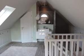 A room with a sloped ceiling, a white door, a small sink, a mirror, and a white railing. - Holiday apartment in Sylt with 1 bedroom (Sylt \/ OT Westerland)