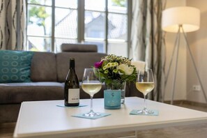A room with a white coffee table, a bottle of wine, two wine glasses, and a vase with flowers. - Holiday home with 3 bedrooms (Ostseebad Zingst a Darß)