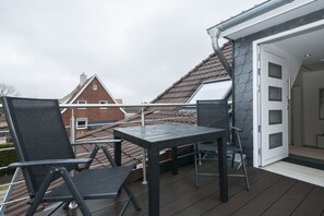 Ein Balkon mit Tisch und Stühlen, eine Tür zum Innenraum und im Hintergrund ein rotes Backsteinhaus.