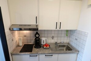 A kitchen with white cabinets, a coffee maker, a kettle, a sink, and a black countertop. - Holiday apartment with 1 bedroom (Burgtiefe auf Fehmarn)