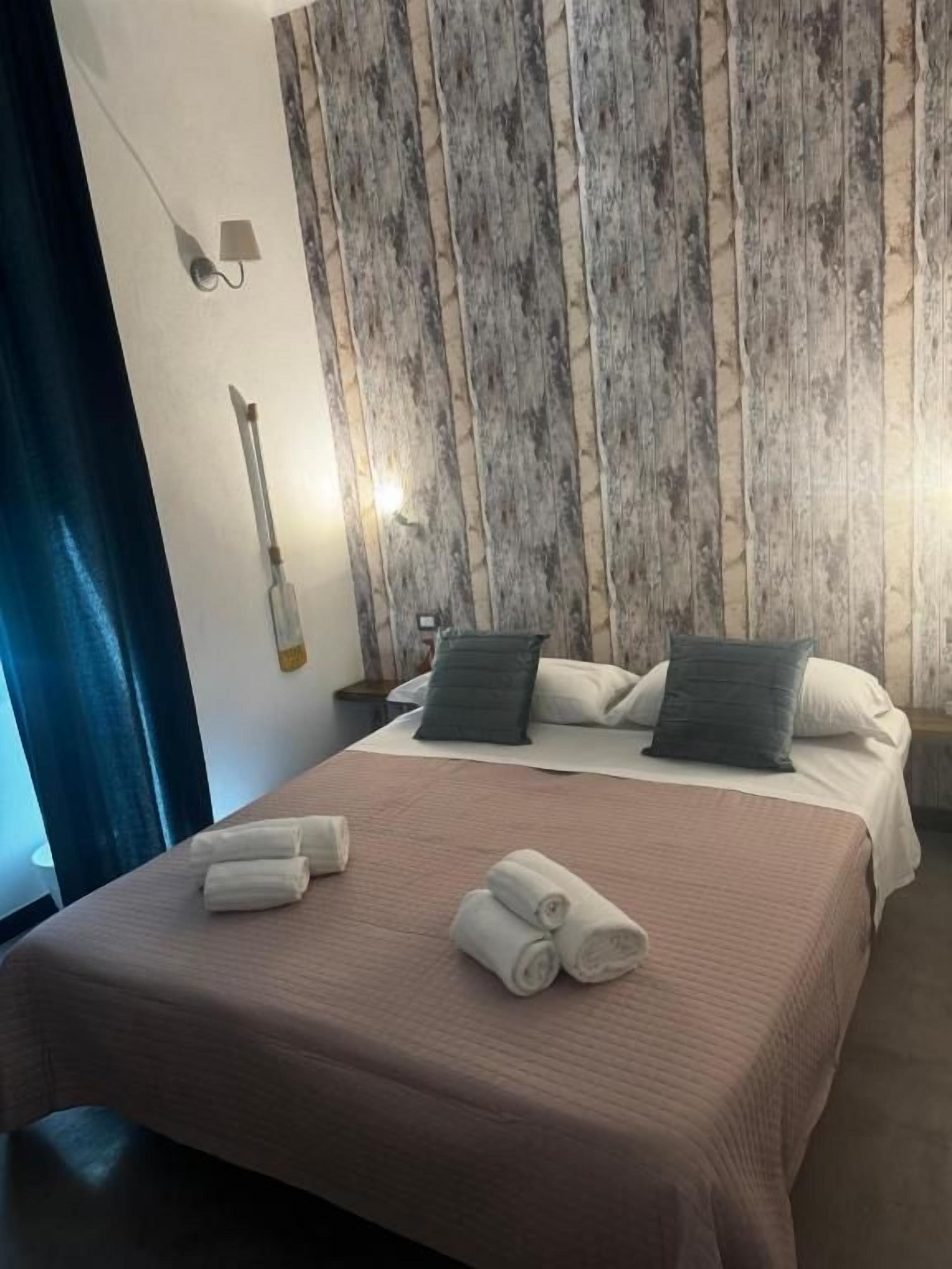 A hotel room with a bed, pillows, and rolled towels on the bed.