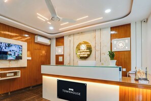 A reception area with a wooden finish, a reception desk, a mounted television, and a sign indicating 'OYO TOWNHOUSE'. - Townhouse Sri Nirvana Grand (Hyderabad)