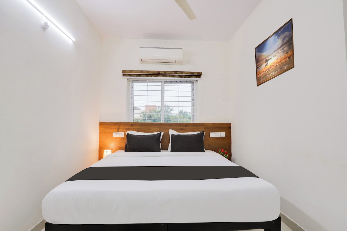 A hotel room with a bed, a window, an air conditioning unit, and a painting on the wall.