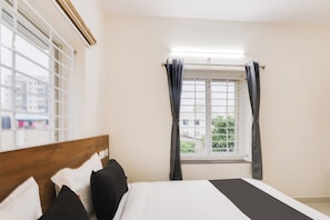 A hotel room with a bed, a window with curtains, and a view of buildings outside. - Townhouse Sri Nirvana Grand (Hyderabad)
