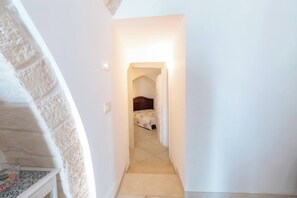 A narrow hallway leading to a bedroom with a bed and a nightstand. - Historic Stone Vault in Noci Incl Breakfast (Noci)