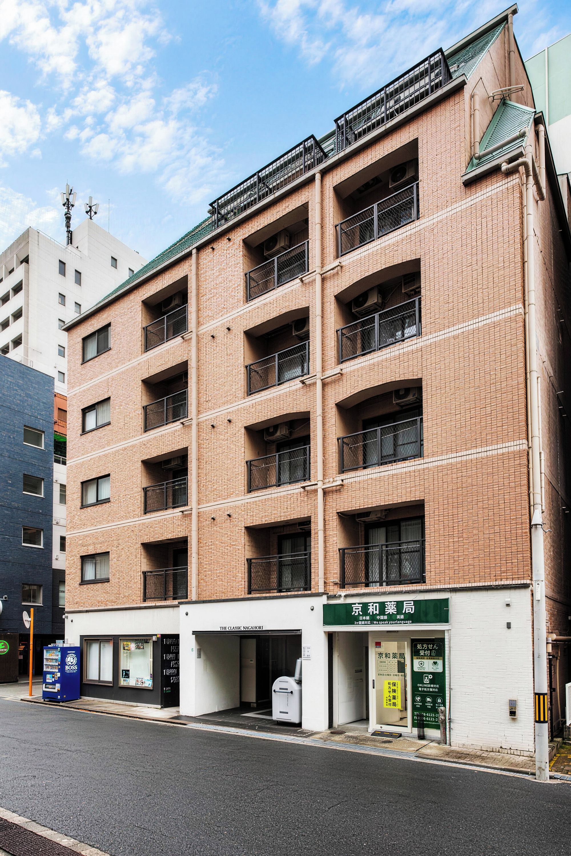 A multi-story building with a brick facade, multiple balconies, and a ground-level entrance with signage.