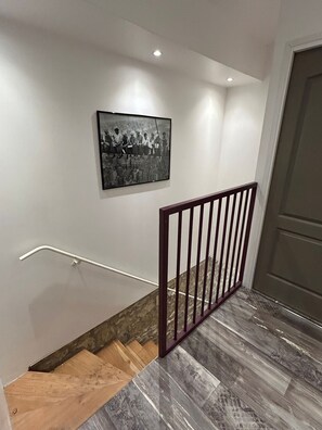 Una escalera con barandilla de madera y pasamanos metálico que conduce a una puerta.