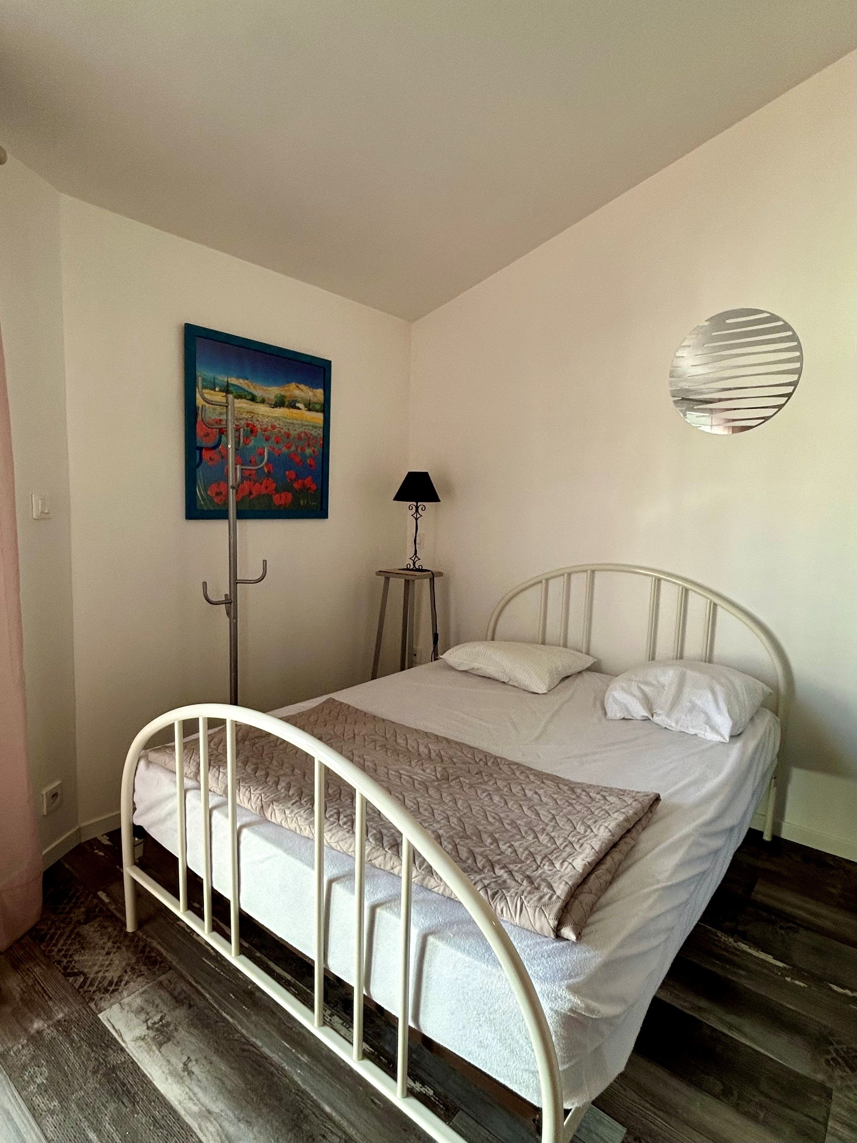 Habitación con cama individual de estructura metálica, un cuadro en la pared, una lámpara de pie y un adorno circular en la pared.