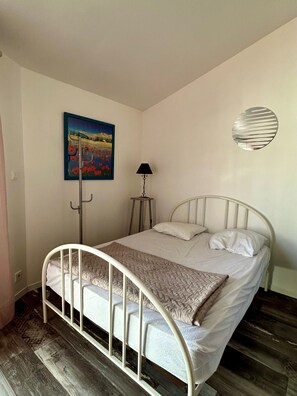 Habitación con cama individual de estructura metálica, un cuadro en la pared, una lámpara de pie y un adorno circular en la pared.