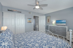 A bedroom with a bed, a dresser, a television, and a ceiling fan. - #203 Curran Shores N. 2/2 Oceanfront Condo (Daytona Beach Shores)