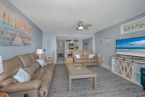 A living room with a beige sofa, a coffee table, and a television on a stand. - #203 Curran Shores N. 2/2 Oceanfront Condo (Daytona Beach Shores)