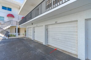 A multi-story residential building with a covered parking area, numbered garage doors, and a staircase leading to an upper level. - #203 Curran Shores N. 2/2 Oceanfront Condo (Daytona Beach Shores)