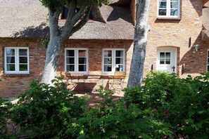 Ein Backsteinhaus mit einem Reetdach, mehreren Fenstern und einer Bank im Vordergrund.