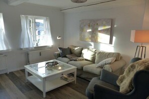 A living room with a sofa, a glass coffee table, a lamp, and a painting on the wall. - Holiday apartment with 1 bedroom (Alkersum)