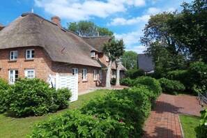 A traditional brick house with a thatched roof, surrounded by well-maintained hedges and a brick pathway. - Holiday apartment with 1 bedroom (Alkersum)