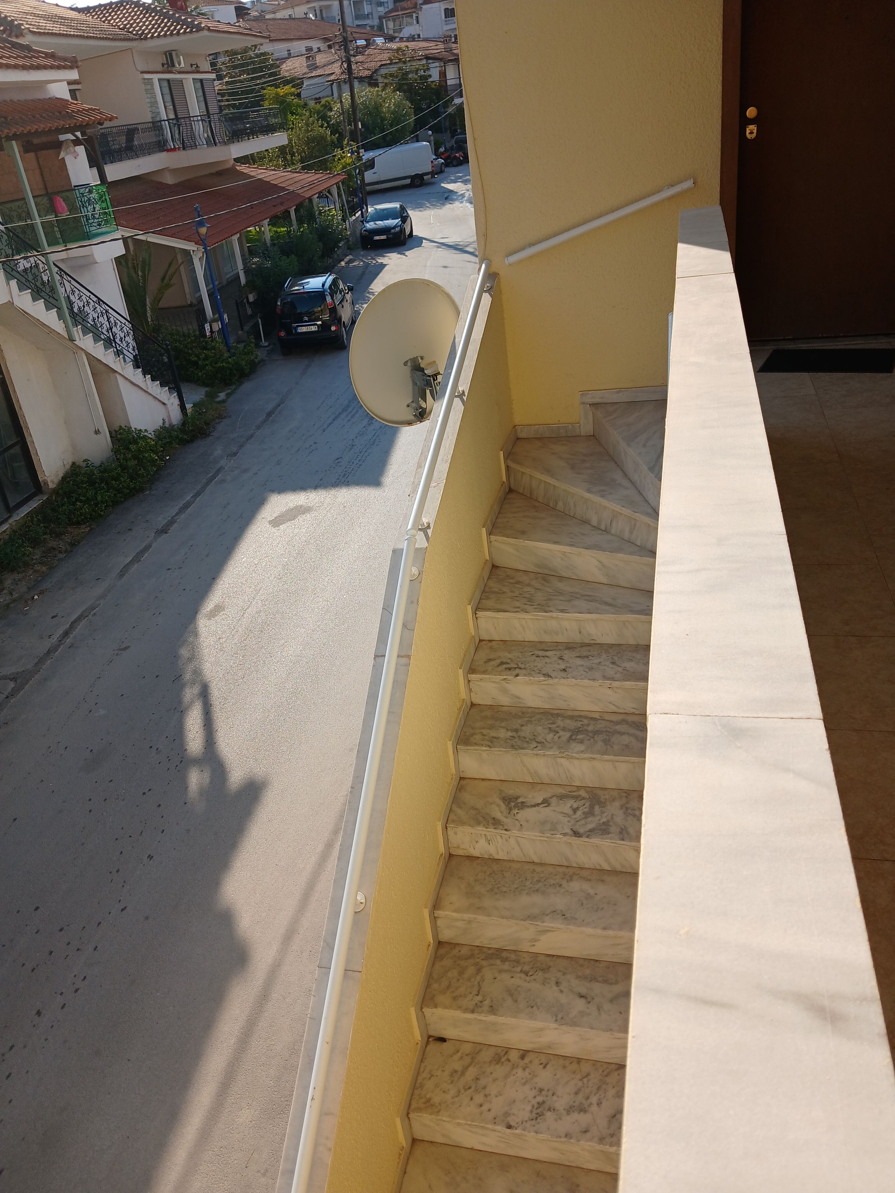 Una calle residencial con un edificio amarillo, una antena parabólica y una escalera.
