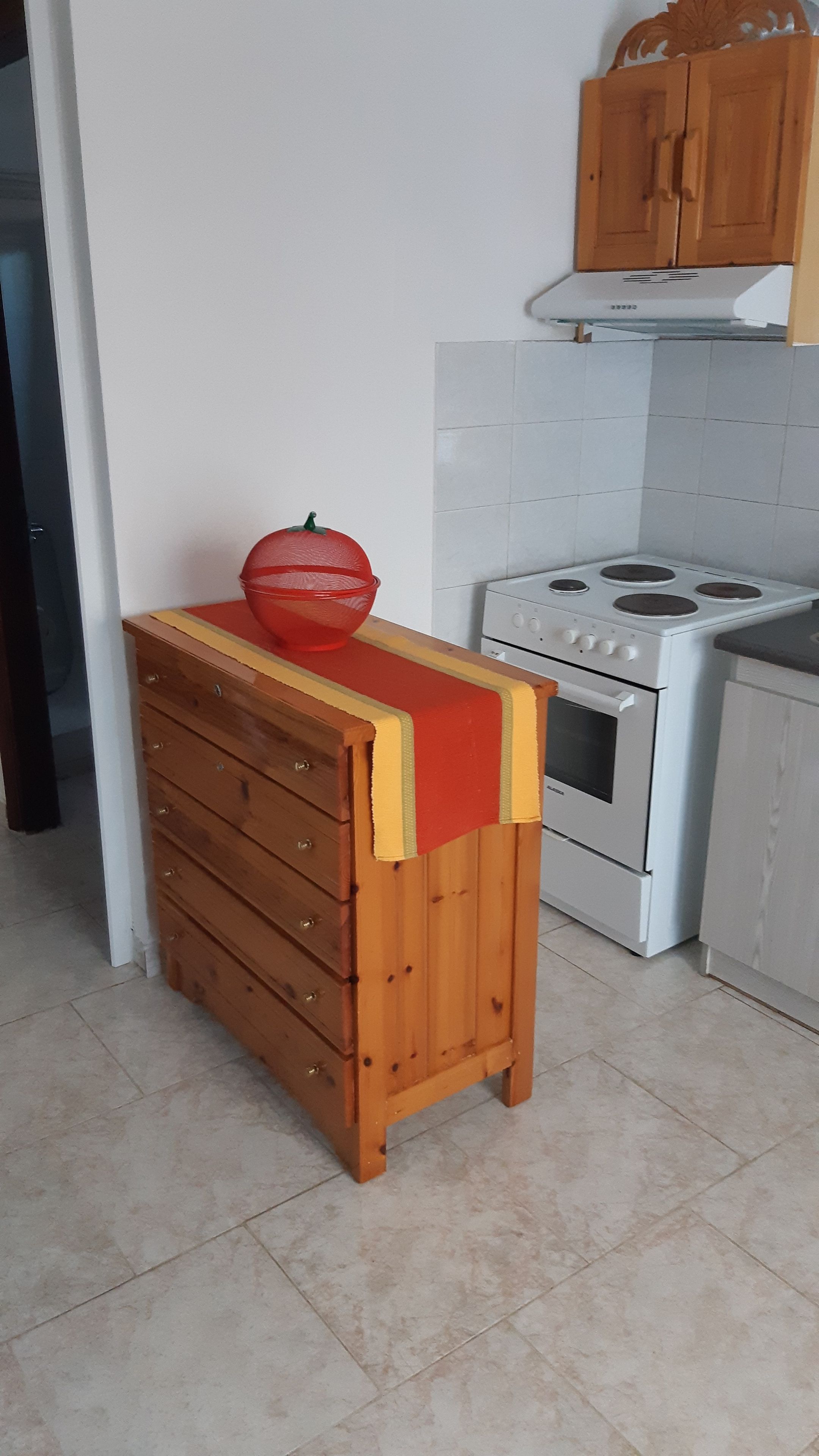 A kitchen with a wooden cabinet, a stove, and a red bowl on a wooden table.