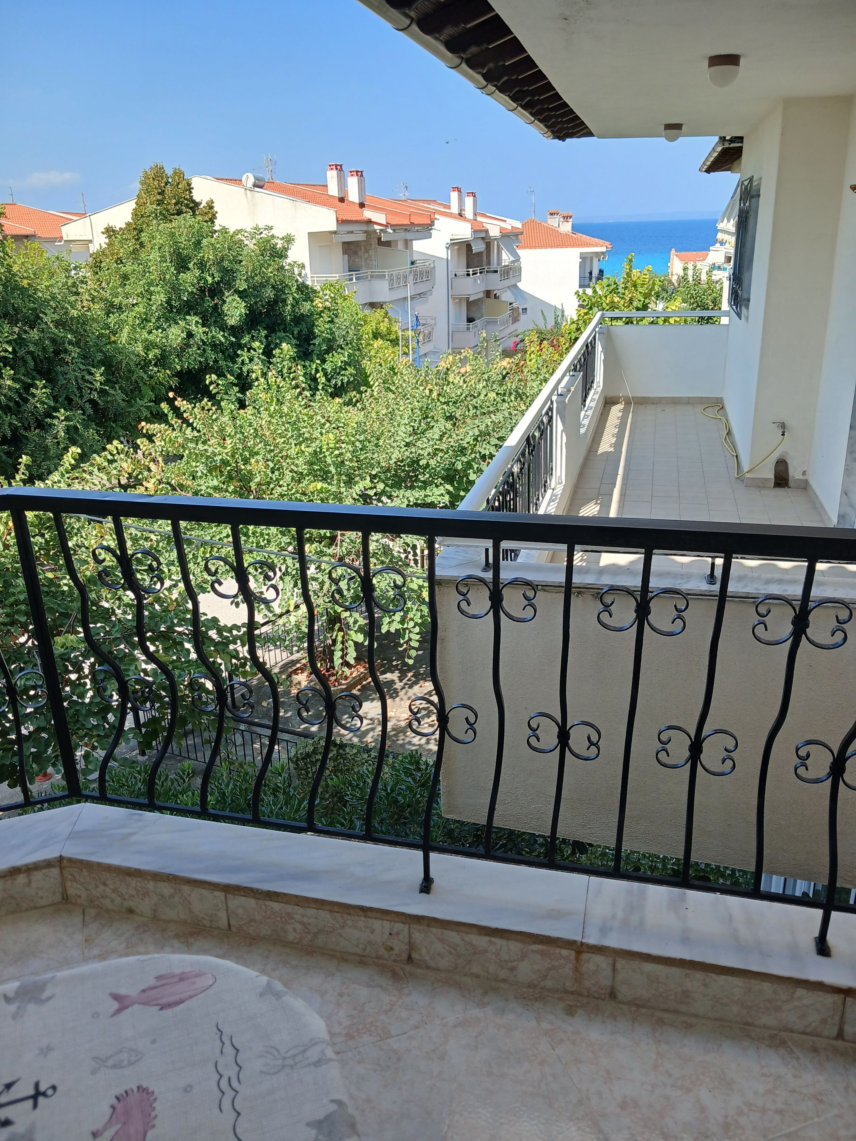 A balcony with a view of the sea, a tiled floor, and a railing.