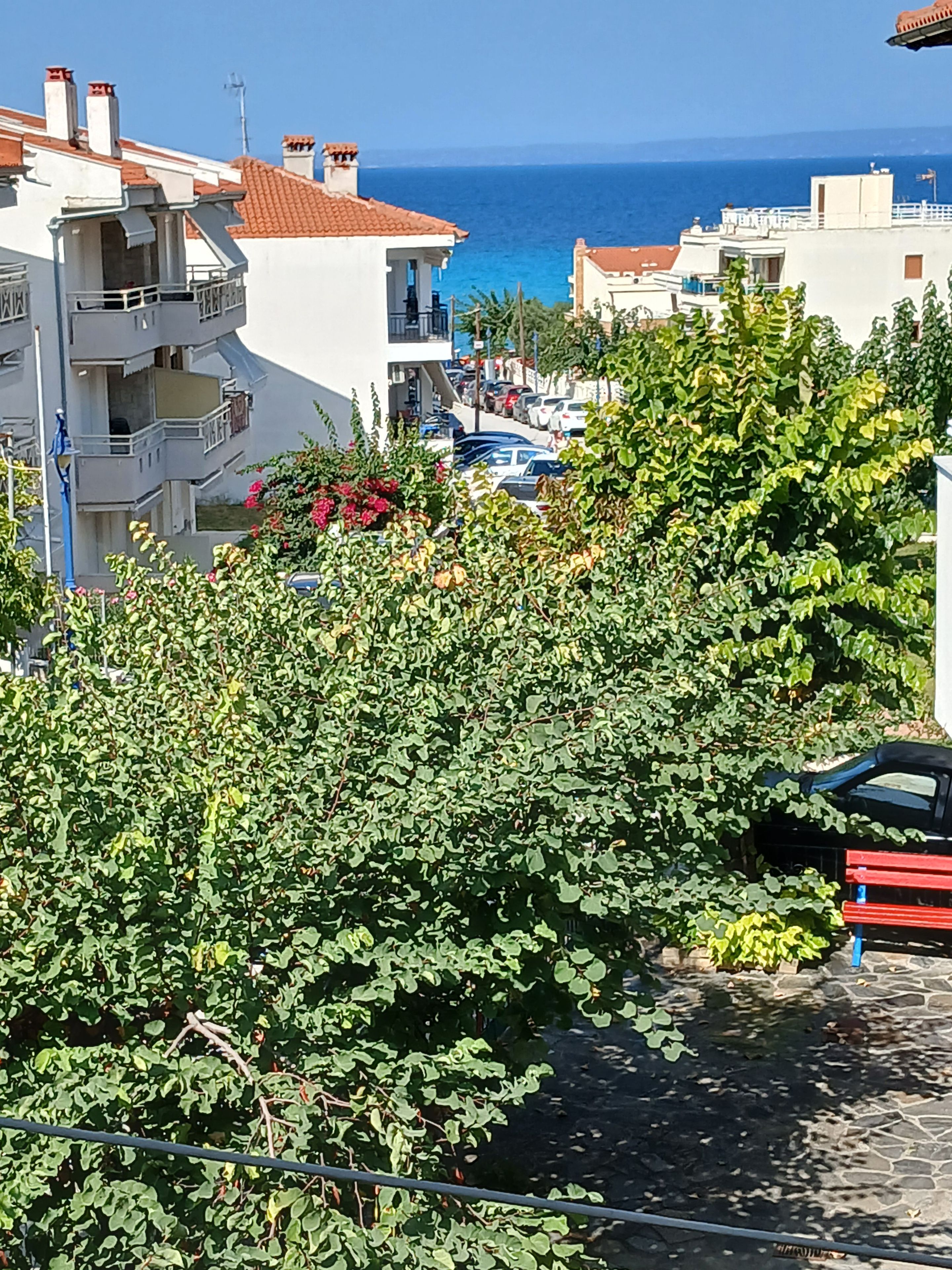 A residential area with a view of the sea, featuring a building with a balcony and parked cars.